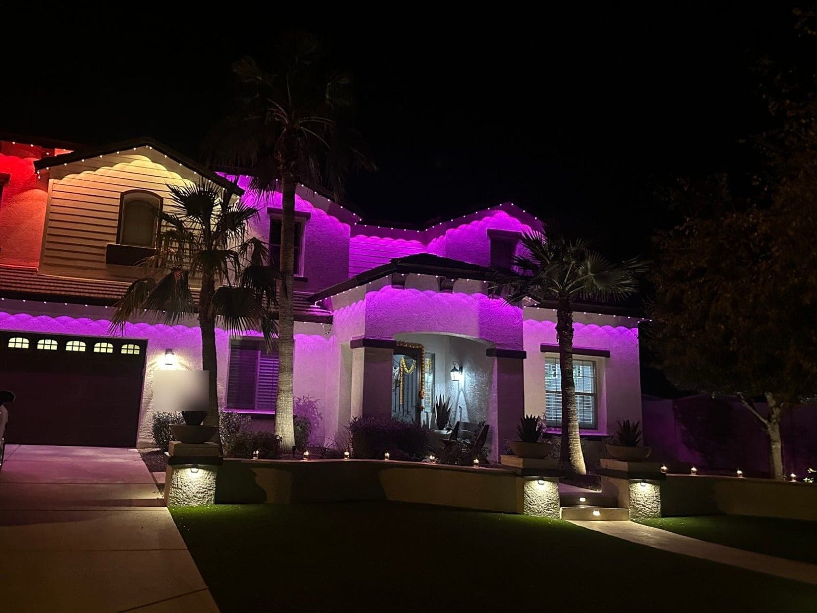 Two-story home glowing pink and purple under its roofline lights at night