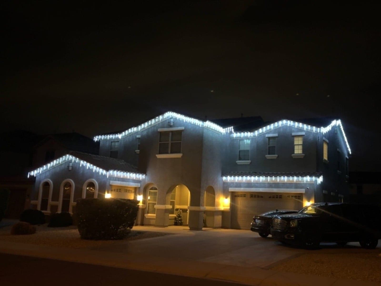 Two-story home outlined in white icicle lights at night